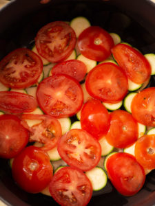 An overhead view of the soup pot to show layered ratatouille ingredients with tomatoes slices on top