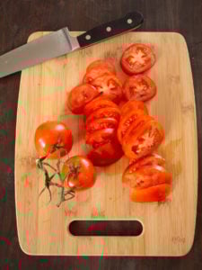 An overhead view of a chopping board to show sliced tomatoes