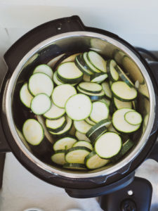 Instant Pot on sauté mode heating sliced zucchini for ratatouille recipe