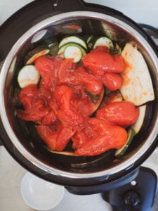 Instant Pot on sauté mode heating sliced zucchini and canned tomatoes for ratatouille recipe