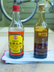 Side-by-side comparison of a bottle of dark soy sauce and light soy sauce on a wood surface