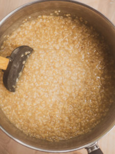 A spatula stirring oatmeal as it thickens while cooking in vegetable stock for the savory oatmeal recipe