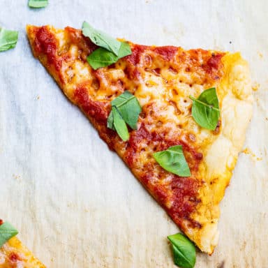 A slice of pizza with cheese, marinara sauce, and fresh basil