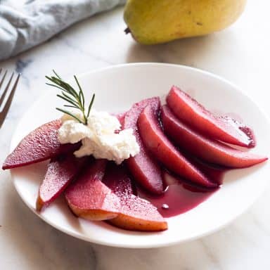 Poached pears on a white plate with a dollop of whipped cream