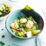 A bowl of cabbage soup with shrimp and tofu in a green bowl
