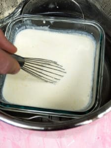A whisk mixing yogurt into the warmed heavy whipping cream