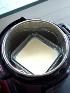 A glass container of heavy whipping cream on a rack in an Instant Pot