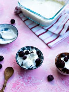 Blueberries and cherries topped with crème fraîche next to a spoon