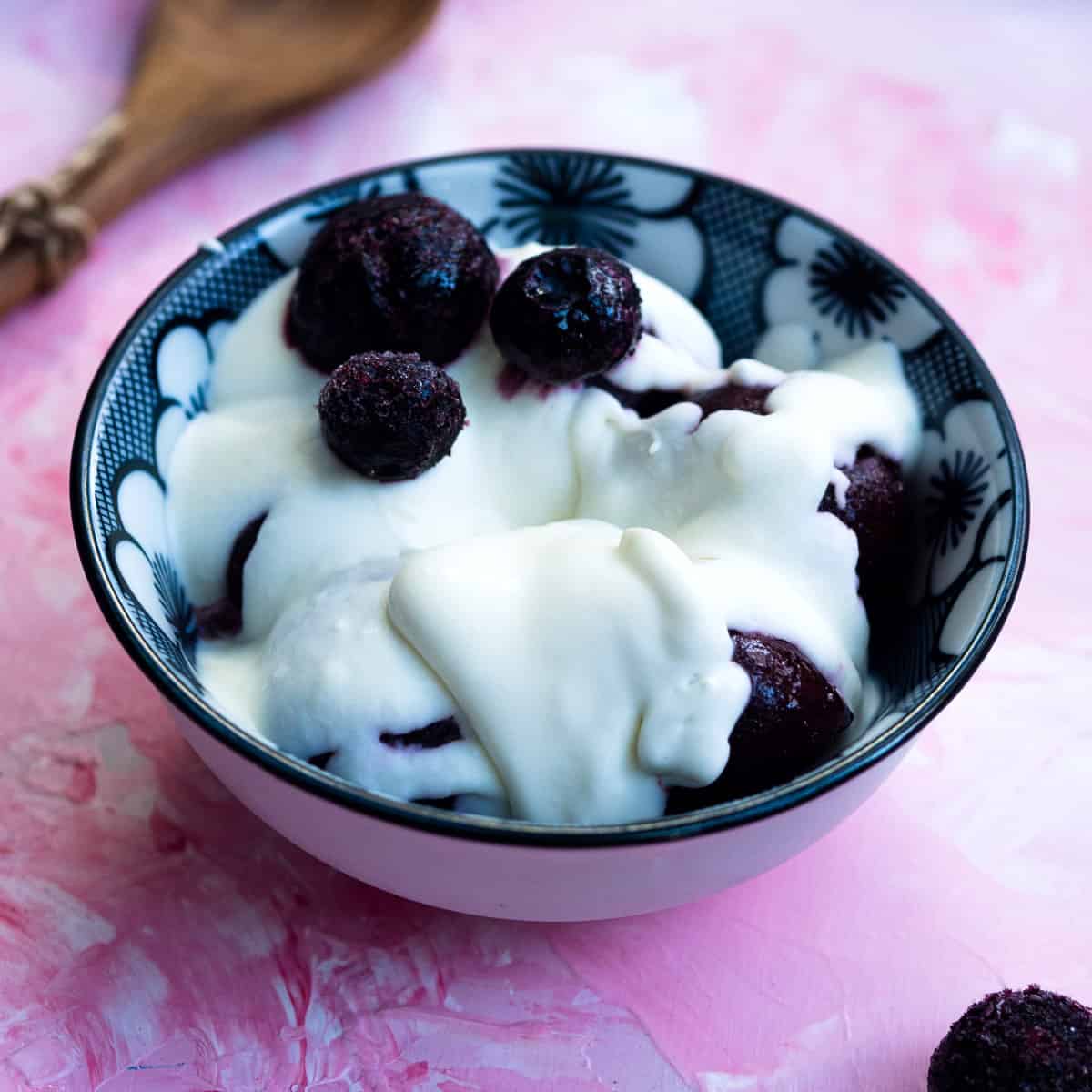 Blueberries and cherries topped with crème fraîche in a blue bowl next to a spoon