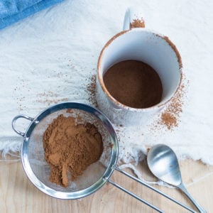 A sieve with cocoa powder and a white mug for the experiment to get rid of clumps from hot cocoa