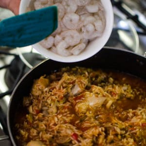 Close up shot of adding shrimp to cooked Jambalaya. Recipe from garlicdelight.com.