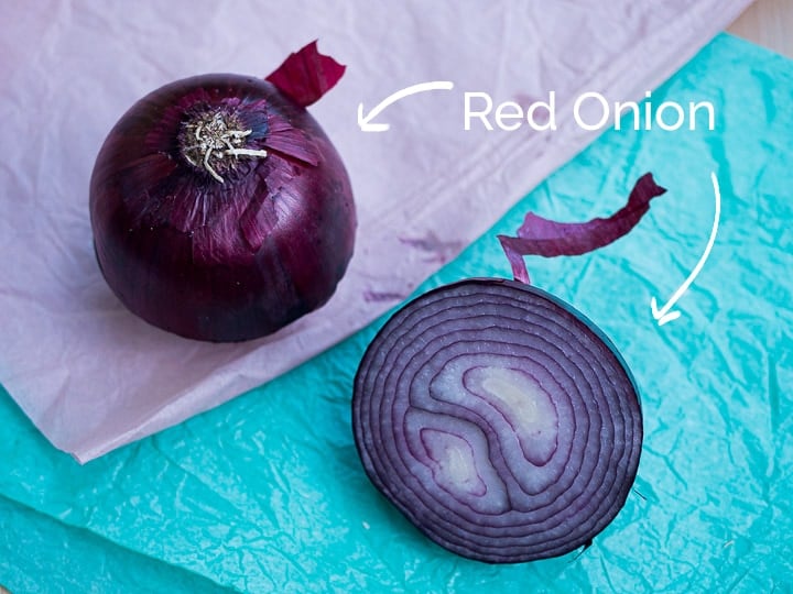 A view of a red onion chopped in half to see the cross sectional view and the outer skin