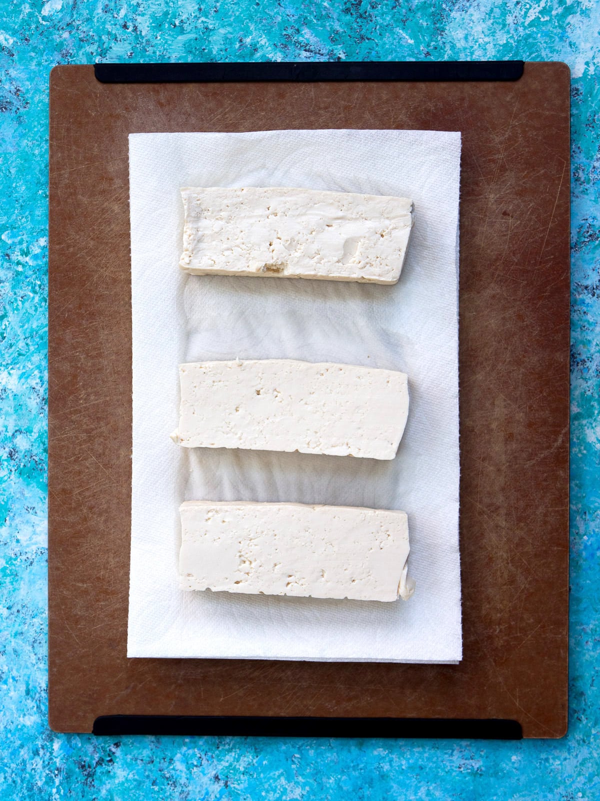 Sliced tofu with paper towels underneath on a chopping board