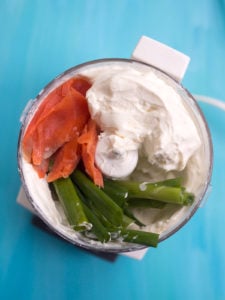 Blocks of cream cheese in a blender with salmon and green onions
