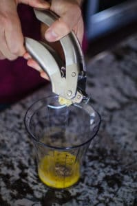 Close up shot of Alex squeezing cloves of garlic with a garlic press. Recipe from garlicdelight.com.