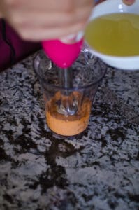 Medium close up shot of pouring oil into immersion blender mix. Recipe from garlicdelight.com.