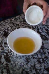 Close up shot of apple cider vinegar in a white bowl with sugar pouring in. Recipe from garlicdelight.com.