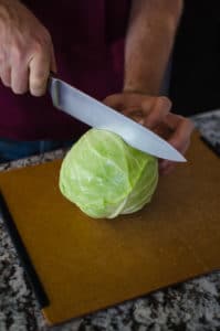 Close up shot of Alex cutting a head of cabbage into halves. Recipe from garlicdelight.com.