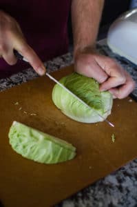 Close up shot of Alex cutting a half head of cabbage into thirds. Recipe from garlicdelight.com.