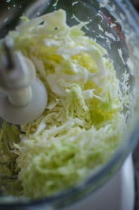 Overhead shot of shredded cabbage in food processor. Recipe from garlicdelight.com.