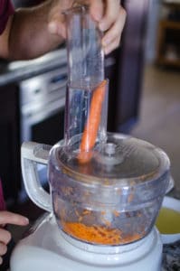 Close up shot of pushing a carrot into food processor. Recipe from garlicdelight.com.